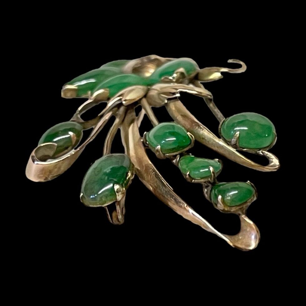 A photo of the jade spray brooch displayed with the longer end in the foreground. The brooch is under the studio light and the jade stones colour is highlighted here.