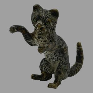 Main photo of small antique bronze cat displayed upright on its backside and facing towards the bottom left corner. Its front right paw is raised as if pawing