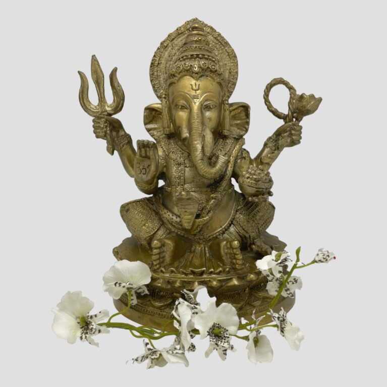 Main photo of antique bronze Lord Ganesh shown against a light grey background and facing forward at the camera. There a spray of white orchids laid around his feet. This bronze has a golden hue and is very well presented.