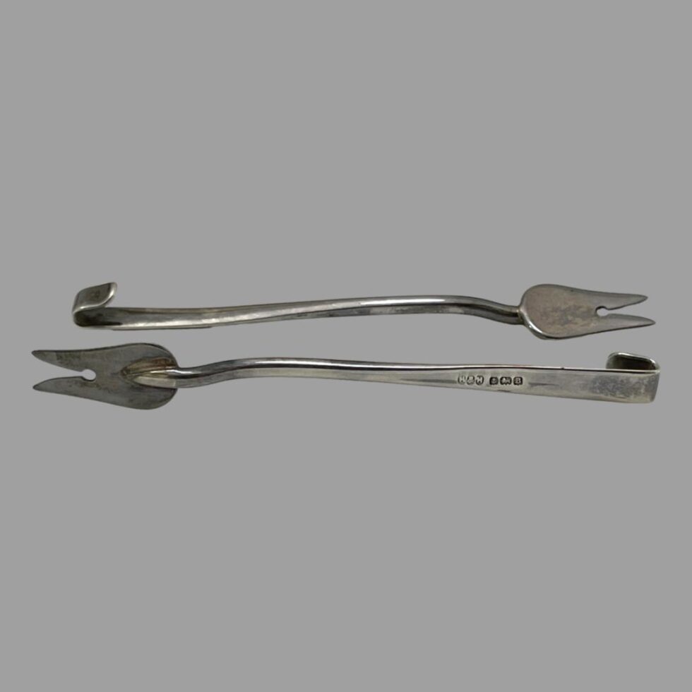 Photo of 2 of the cocktail forks laid head to tail horizontally. The fork in the foreground is on its side with the full hallmark on display to the back of handle. The fork in background is laid flat.