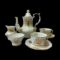 Main photo of Hammersley tea service for 2 displayed against a black background with the tea/coffee pot at the centre back, milk jug to its left and sugar bowl in front of the jug. On the right are the 2 cups and saucers one in front of the other. The tea/coffee pot is tall with a bulbous area at the bottom only. The spout protrudes from this area and reaches up to the same level as the rim at top. The lovely curved handle starts at the top rim, extends slightly above the rim and then downward finishing on the bulbous lower area. The set is white with gilt rose decorations known as the Golden Glory pattern and gilt around the rims and handles. It is in very good condition for its age. Lovely gift item for a wedding anniversary or wedding.