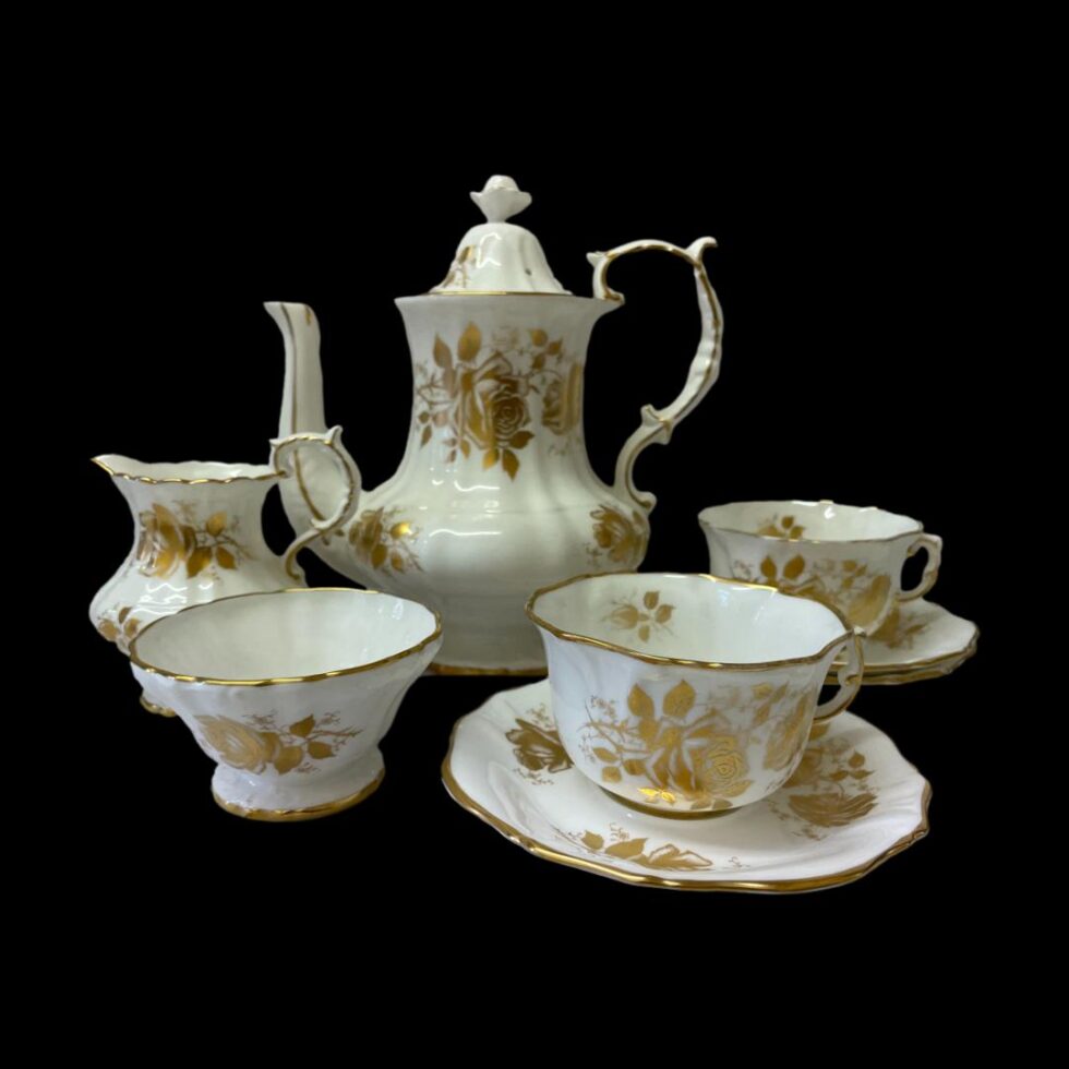 Main photo of Hammersley tea service for 2 displayed against a black background with the tea/coffee pot at the centre back, milk jug to its left and sugar bowl in front of the jug. On the right are the 2 cups and saucers one in front of the other. The tea/coffee pot is tall with a bulbous area at the bottom only. The spout protrudes from this area and reaches up to the same level as the rim at top. The lovely curved handle starts at the top rim, extends slightly above the rim and then downward finishing on the bulbous lower area. The set is white with gilt rose decorations known as the Golden Glory pattern and gilt around the rims and handles. It is in very good condition for its age. Lovely gift item for a wedding anniversary or wedding.