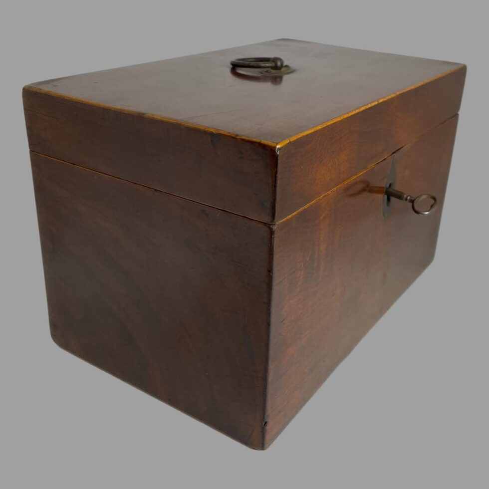 Photo of small antique tea caddy seen with lid closed, key in its slot and from a corner angle with the front to the right and one side on the left.