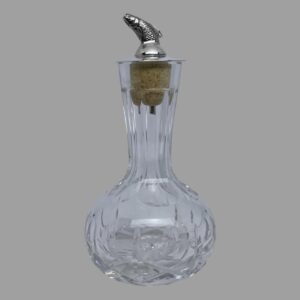 Main photo of silver &crystal bitters bottle seen from an eye level with the leaping salmon facing left. The crystal bottle has a short slender neck and a bulbous bottom making it easy to grip. The salmon dasher appears to leap out of the top like a real life leaping salmon with just the dorsal fin upward sticking out of a smooth silver top. There is quite a bit of detail to the salmon with scales and gills.