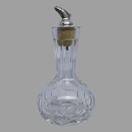 Main photo of silver &crystal bitters bottle seen from an eye level with the leaping salmon facing left. The crystal bottle has a short slender neck and a bulbous bottom making it easy to grip. The salmon dasher appears to leap out of the top like a real life leaping salmon with just the dorsal fin upward sticking out of a smooth silver top. There is quite a bit of detail to the salmon with scales and gills.