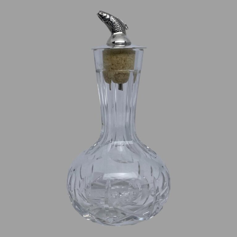 Main photo of silver &crystal bitters bottle seen from an eye level with the leaping salmon facing left. The crystal bottle has a short slender neck and a bulbous bottom making it easy to grip. The salmon dasher appears to leap out of the top like a real life leaping salmon with just the dorsal fin upward sticking out of a smooth silver top. There is quite a bit of detail to the salmon with scales and gills.