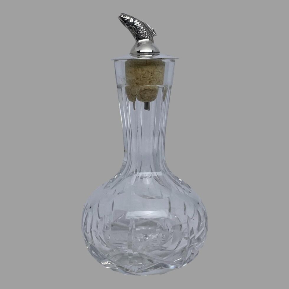 Main photo of silver &crystal bitters bottle seen from an eye level with the leaping salmon facing left. The crystal bottle has a short slender neck and a bulbous bottom making it easy to grip. The salmon dasher appears to leap out of the top like a real life leaping salmon with just the dorsal fin upward sticking out of a smooth silver top. There is quite a bit of detail to the salmon with scales and gills.