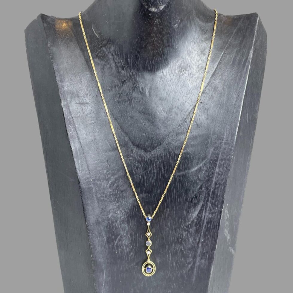 Photo of gold sapphire necklace displayed on a black wooden display stand with the necklace front forward facing.
