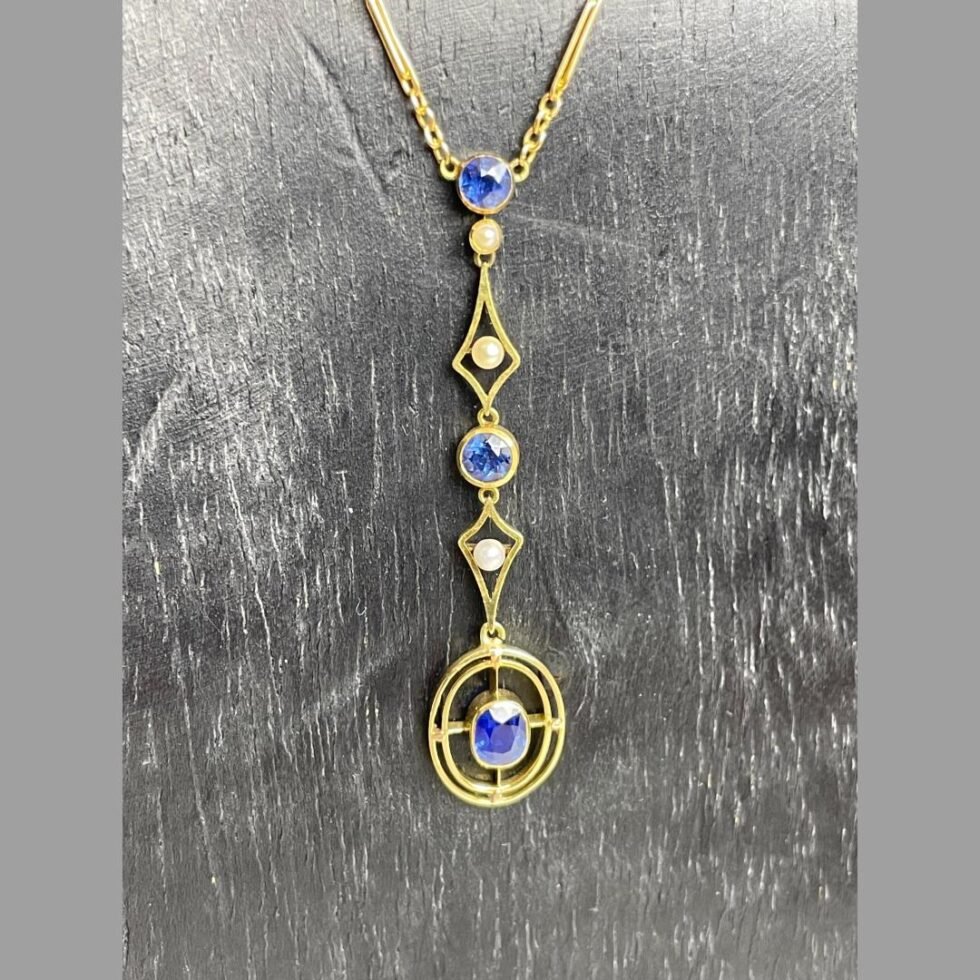 Photo of the attached pendant area of antique gold &sapphire necklace in close up displayed hanging from a black wooden stand.