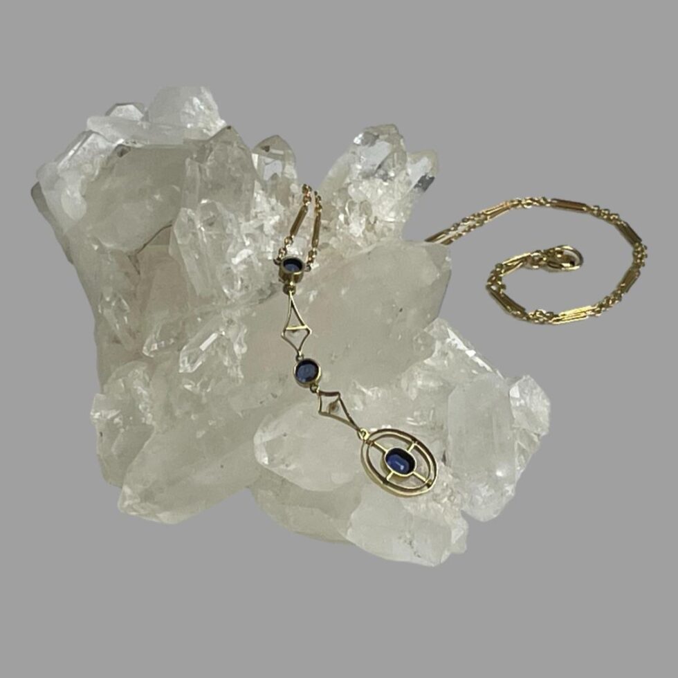 Photo of the gold & sapphire necklace shown with the back of the attached pendant area on display on top of a rock of natural quartz crystal.