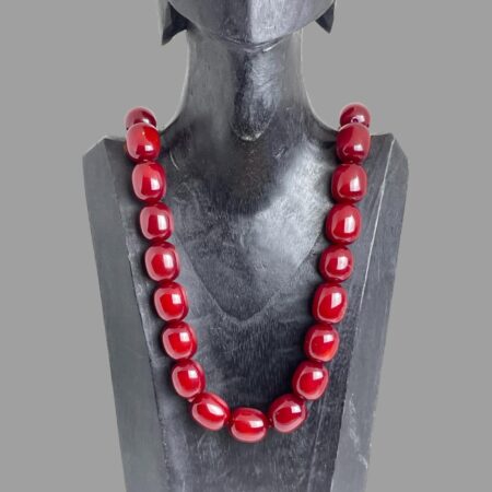 Main photo of cherry bakelite amber necklace displayed on a black wooden display stand and forward facing. The beads of this necklace are large barrel shaped and the colour is absolutely cherry red!