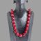 Main photo of cherry bakelite amber necklace displayed on a black wooden display stand and forward facing. The beads of this necklace are large barrel shaped and the colour is absolutely cherry red!