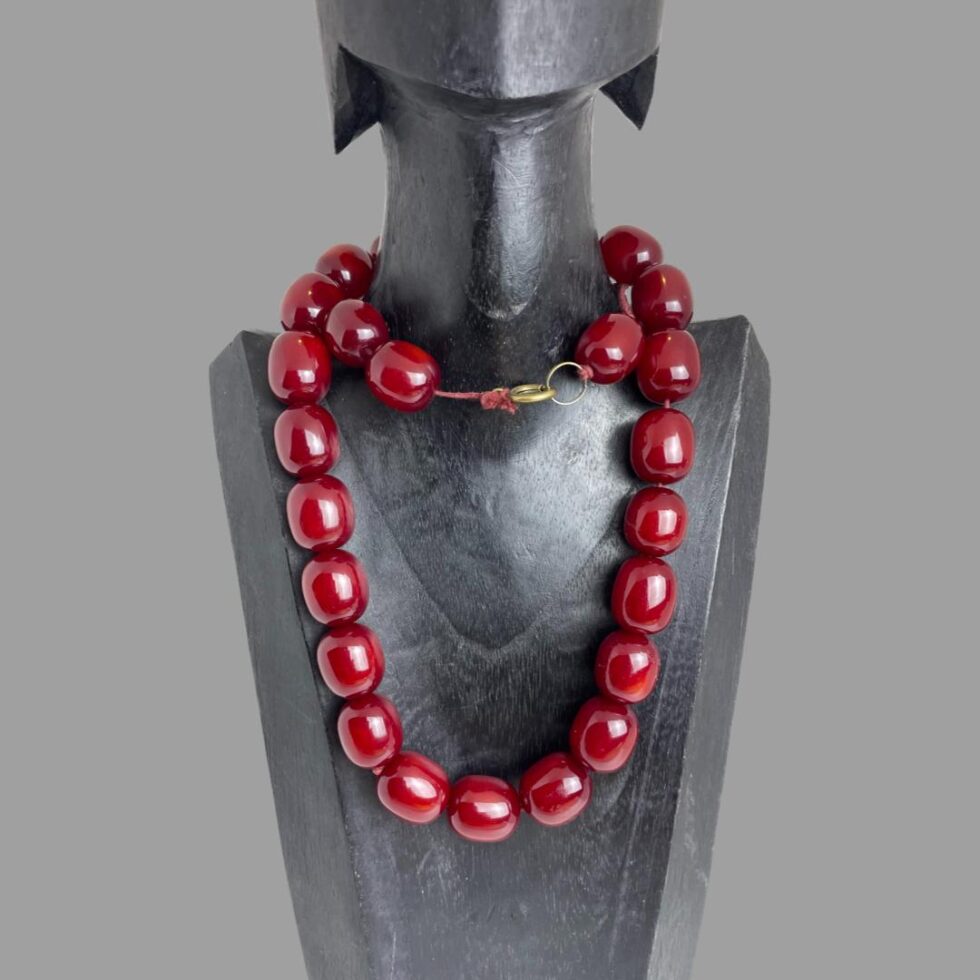 Photo of cherry amber bakelite necklace still displayed on a black wooden stand and wound round once around the neck to show the clasp in the centre top. The loosening string especially around the clasp area is visible.