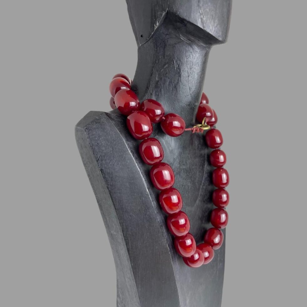 Photo of cherry amber bakelite necklace still on a black wooden display stand with the necklace wound round once around the neck and the front of display facing towards the right.