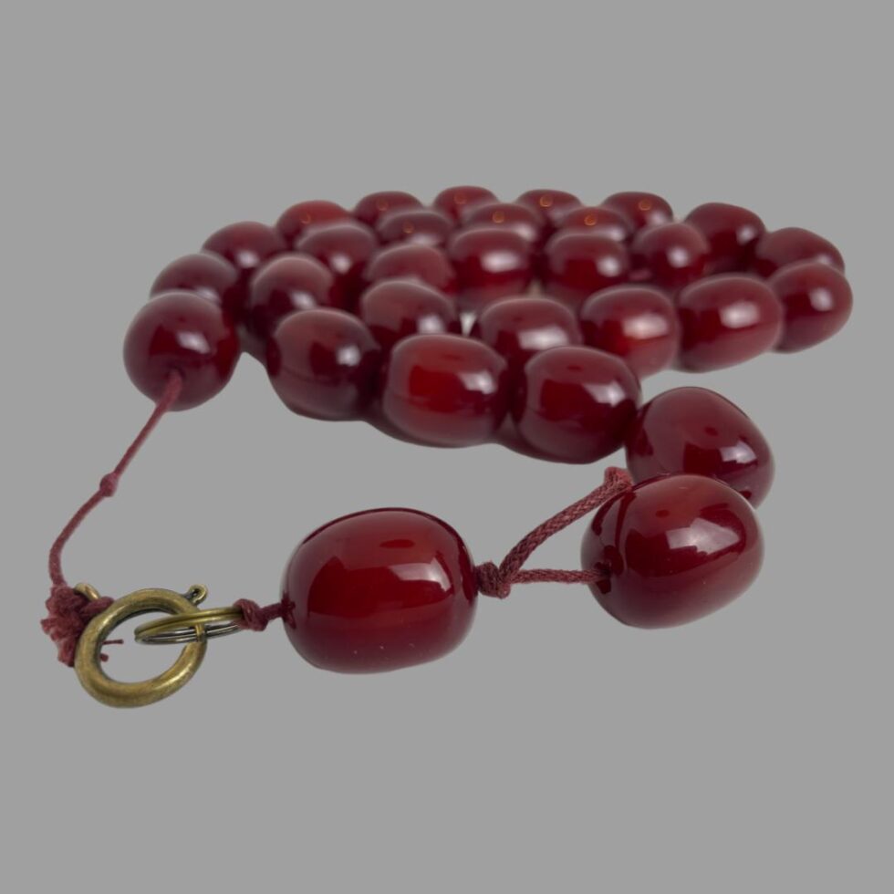 Photo of the cherry amber bakelite necklace displayed on a flat surface with the loose string around the clasp area in the foreground.
