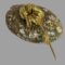 Main photo of signed Dior flower brooch displayed with flower head leaning on an upturned shell. The stem of the flower is quite long and rests on the flat surface. The flower head and leaves are constructed from strands of gilt metal almost hairlike quality
