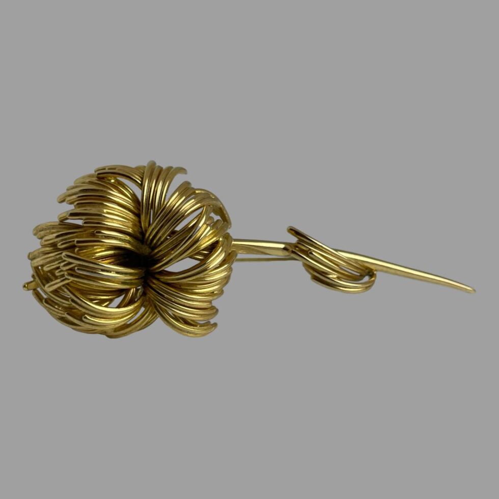 Photo of Dior flower brooch displayed on a flat surface on its side with the pin propping up the brooch to show the front.