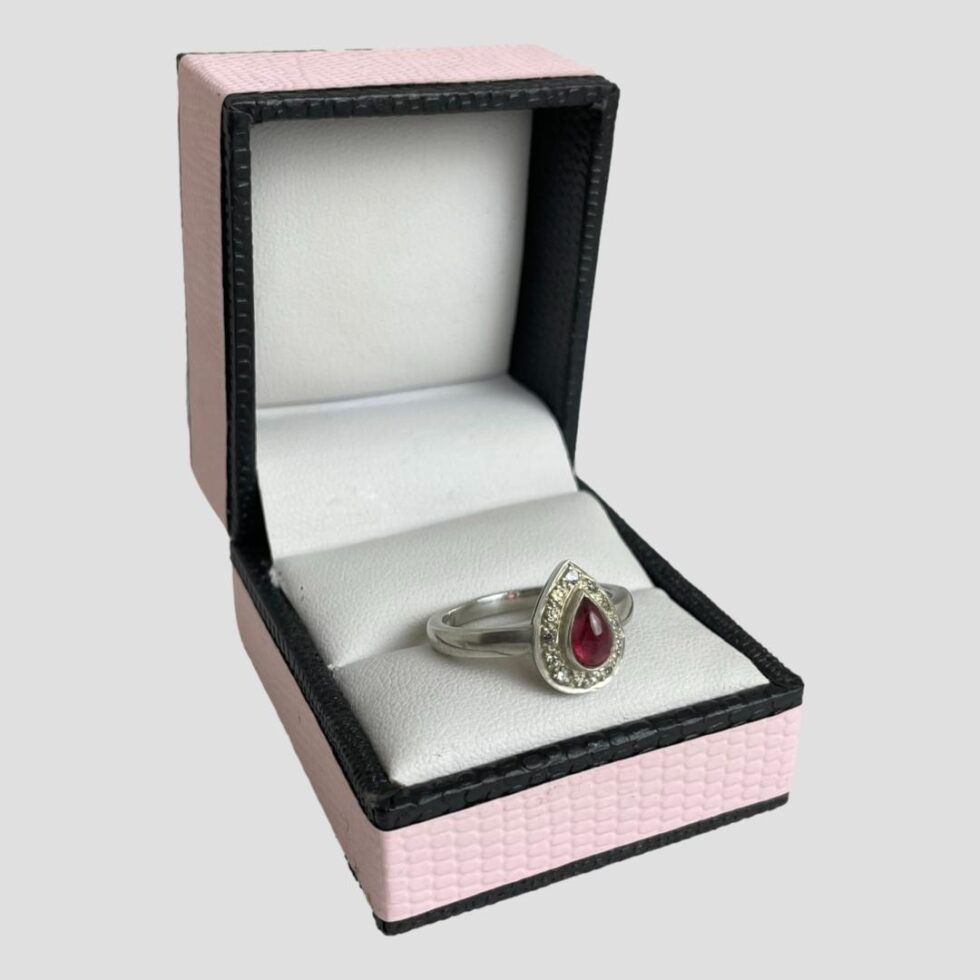 Photo of tourmaline and sapphire ring still displayed inside its ring box this time with the ring front facing towards the bottom right corner.