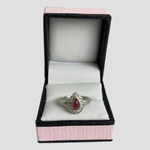 Main photo of tourmaline & sapphire ring displayed inside its ring box which has a baby pink colour exterior with black beading. The ring is forward facing with the pointed end at the top.