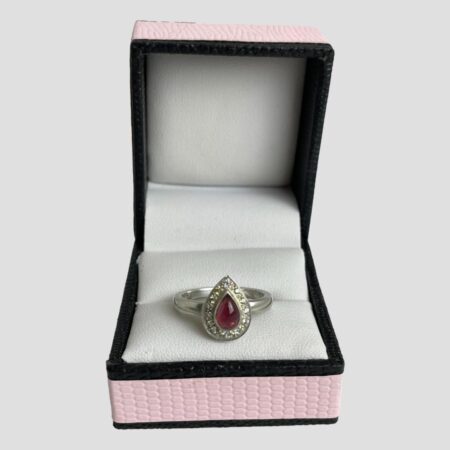 Main photo of tourmaline & sapphire ring displayed inside its ring box which has a baby pink colour exterior with black beading. The ring is forward facing with the pointed end at the top.