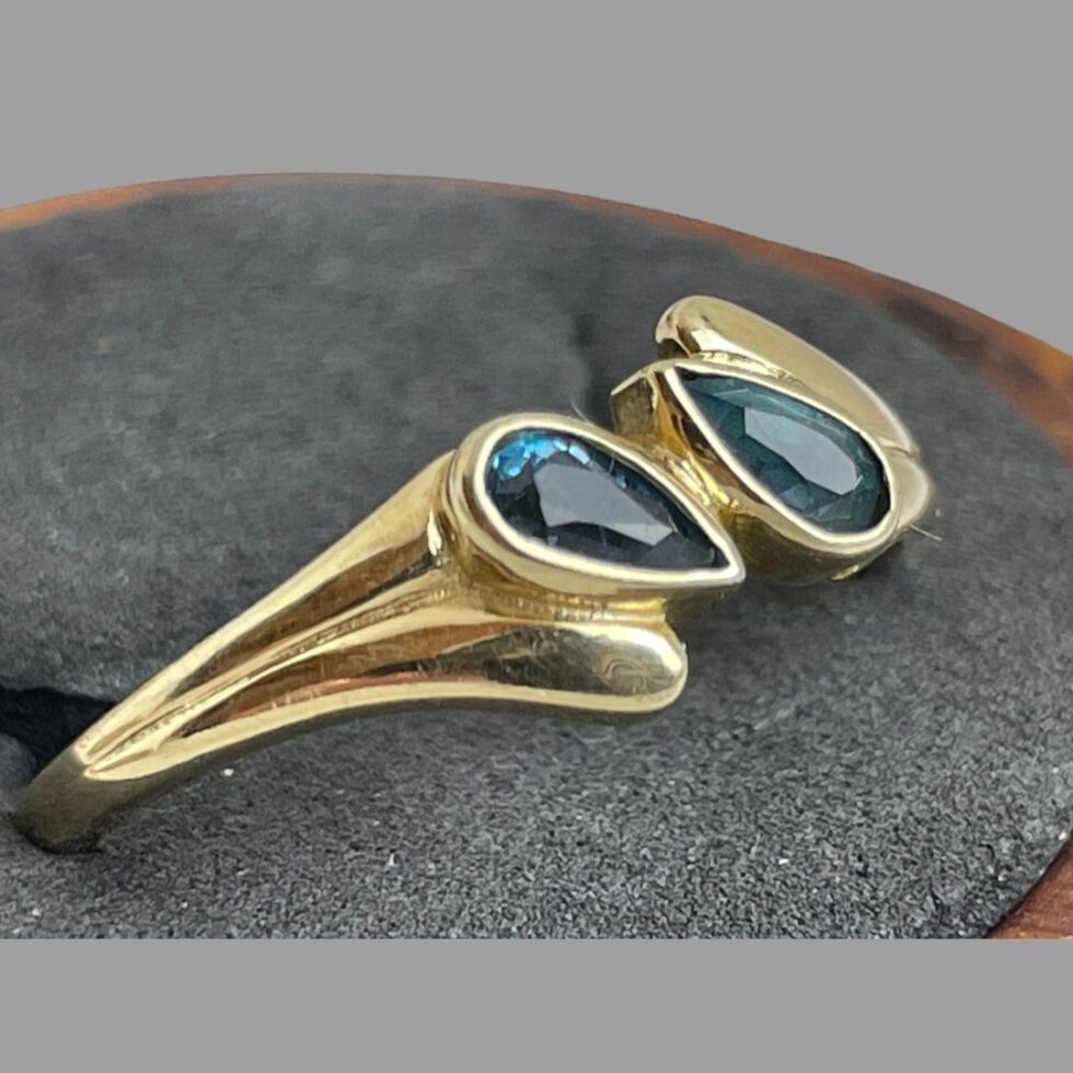 A close up photo of the gold blue gemstone ring shown from a side angle highlighting the shoulder design of the ring band and the stone setting. From this angle the stones appear as different shades of blue.