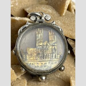 Main photo of Victorian Westminster souvenir fob displayed on a rock of desert sand rose with the iconic west entrance of the abbey with the 2 symmetrical towers on display with one side also visible.. Below the gilt image it is written Westminster Abbey. The outer edge of the fob has small silver balls distributed evenly with the gilt abbey image encased in glass on both sides. Although this is a fob, it could just as well be worn on a chain around the neck and would make an unusual pendant.