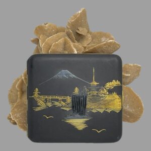 Main photo of Japanese damascene cigarette case displayed upright leaning against a rock of sand rose with the decorative side on display. The image is of Mount Fuji in the background with silver top and a boat with tall sails also in silver in the centre. The rest of the scene is in 24 karat gold inlay showing a pagoda in the background on right, with temple and old thatch houses and trees. On the left is a wooden bridge, some more trees. In very good condition for its age with no dents and only minor signs of wear namely scuff marks to the blackened metal base.