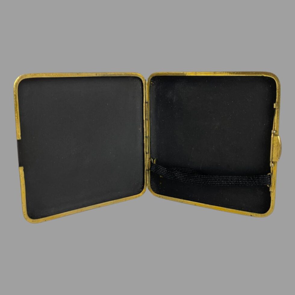 Photo of damascene cigarette case shown open and upright. The inside is very clean and the elastic, which is black, is just visible on the bottom right.