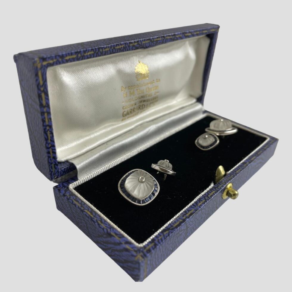 Photo of white gold sapphire cufflinks still displayed inside the box this time with the box front facing towards the bottom right corner of photo.