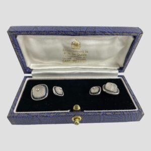 Main photo of white gold sapphire cufflinks displayed inside the Garrard & Co cufflinks box. The open box is forward facing with the cufflinks securely in place to the left and right. The box has a blue exterior, an almost black blue velvet inner and white silk lined inside the lid with Garrard & Co details in gilt. The larger of the link squares are on the outer extremes and the smaller squares inside. The cufflinks design - all uniform except size - square shaped but with rounded edges. A carved rock crystal sits in the centre of each also round-cornered squares. The carving in the crystal is lines emanating from the small round cut diamond at the centre. Around the perimeter is a frame of Channel set sapphires and all set in 18 karat white gold. Each area, the diamond, the rock crystal and the sapphires are separated with a white gold frame - the frame around the diamond is plain white gold whereas the frames around the rock crystal and sapphires have notches all the way around. An incredibly striking pair of cufflinks for the discerning man in your life!