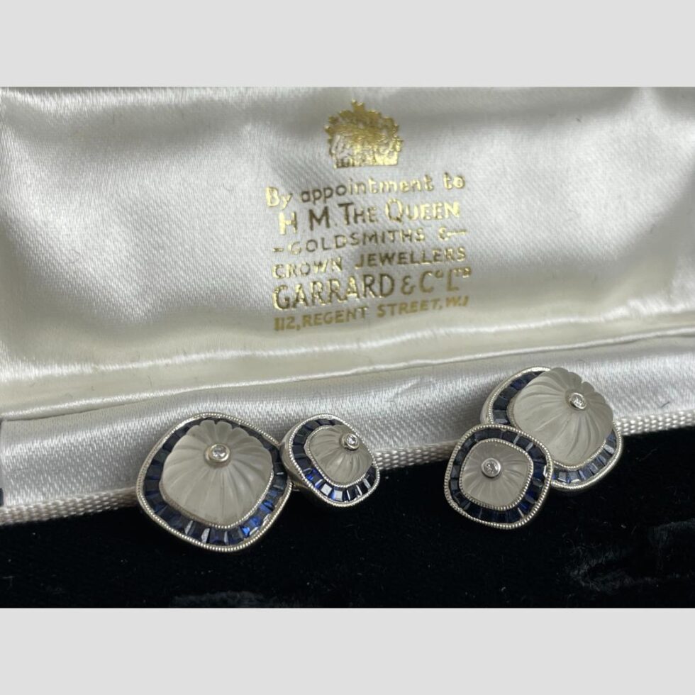 Close up photo of the cufflinks which have beend removed from their fitted secure slots and placed just below the Garrard & Co writing on the inside id.