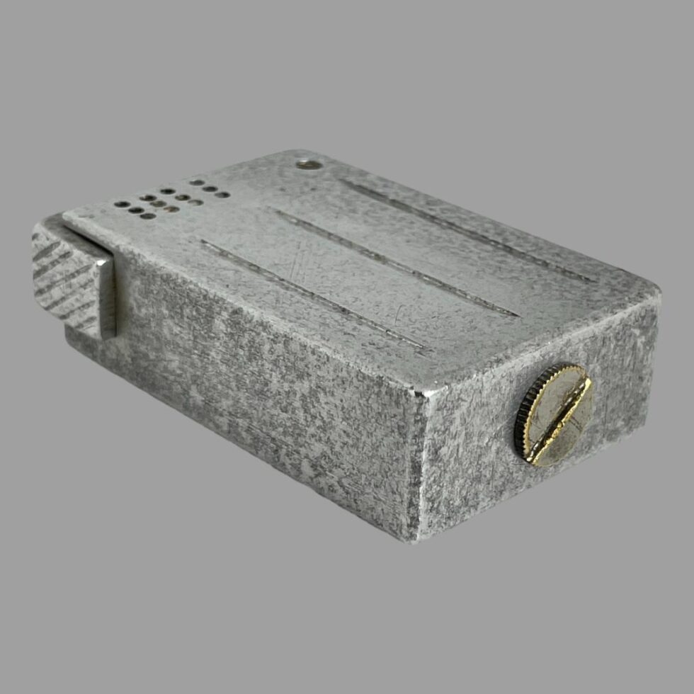 Photo of trench art light displayed flat with the JW side face down. The base of the lighter is facing the bottom right with a brass screw which is where the fuel goes in. The screw is not flush to the base so although the lighter stands upright, it is a little wobbly. The lift arm side is facing the bottom left. It is very evident how solid this lighter is and how it has stood the test of time.