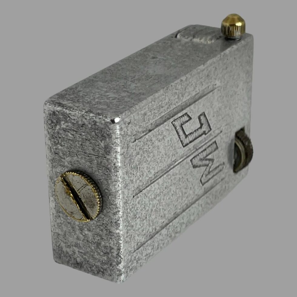 Photo of trench art lighter displayed on its side with the JW initialled side facing towards the right. The brass screw fuel area is in the foreground and to the left and the brass tip for the flint is visible at the top right. This really is a chunky lighter.