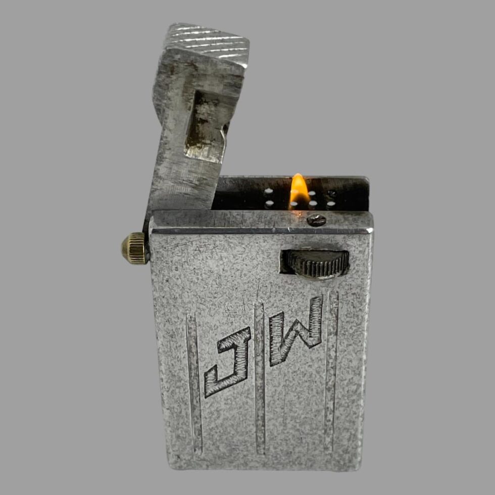 Photo of trench art aluminium lighter displayed with JW side in the foreground. The lift arm is open and the lighter is lit ! (Small flame appearing out of the black abyss)