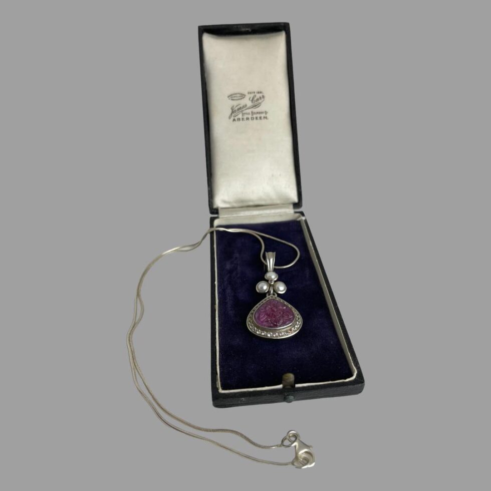 Photo of the ruby sapphire pendant &chain displayed inside the old jewellery box with the chain laid out in a curve outside and to the left of the box.