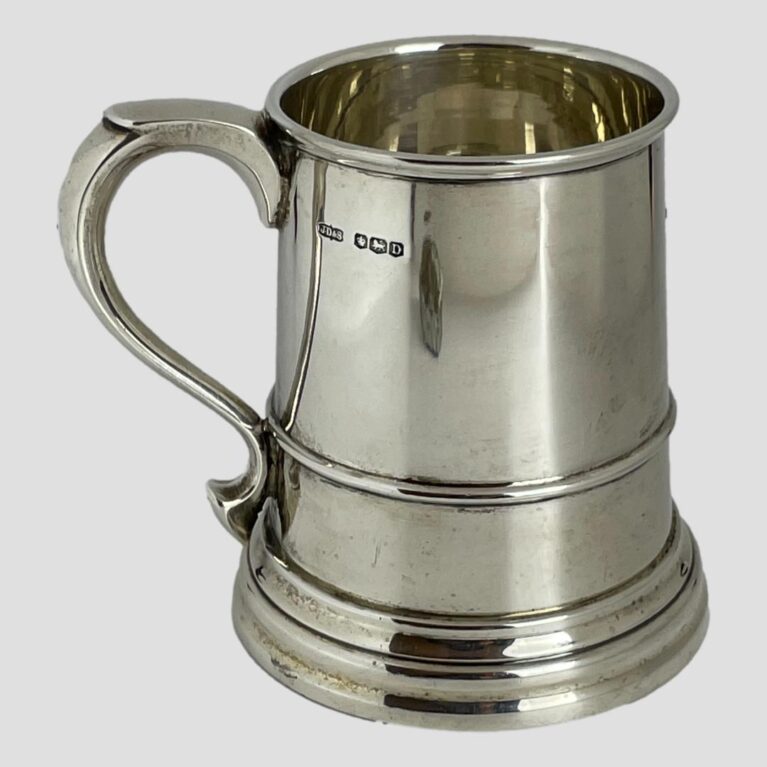 Main photo of silver half pint tankard displayed with the handle on the left and the full hallmark visible on the top right of handle. The tankard is slightly flared at the base making it a sturdy holder of your favourite beer, ale, stout or cider even. The tankard is in very good condition with no damage - almost like it has never been used. Lovely gift item to someone who'll appreciate quality or, as a gift to yourself!