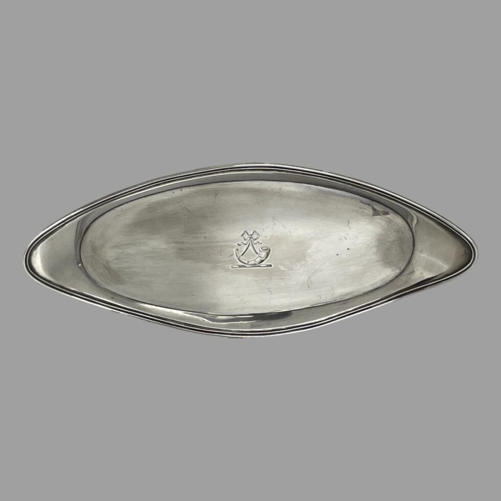 Main photo of George III snuffer tray displayed horizontally upright to show the shape of the tray which is an elongated oval with turned up or raised border. It is almost an eye or almond shape. The crest at the centre is visible which is a ribbon with what looks like a hunters horn of a stand (could be an old hearing aid horn!) Not a lot of use for snuffer trays these days but this could be utilised as an stick incense burner stand as it is long enough. Whatever you decide to use it for, it will be a useful and practical (as well as collectable) item of antique silver.