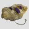 Main photo of purple Mojave turquoise set displayed on a rock of natural river quartz. The pendant on the necklace is at the centre with the chain swirled round to the left and the clasp area to the right in front of the rock. The earrings are flanked to the left and right of the pendant. The purple Mojave turquoise is like a patchwork of different purple shades. In addition to the purple shades, there are flecks of copper prominent mostly in one of the earrings on the left.