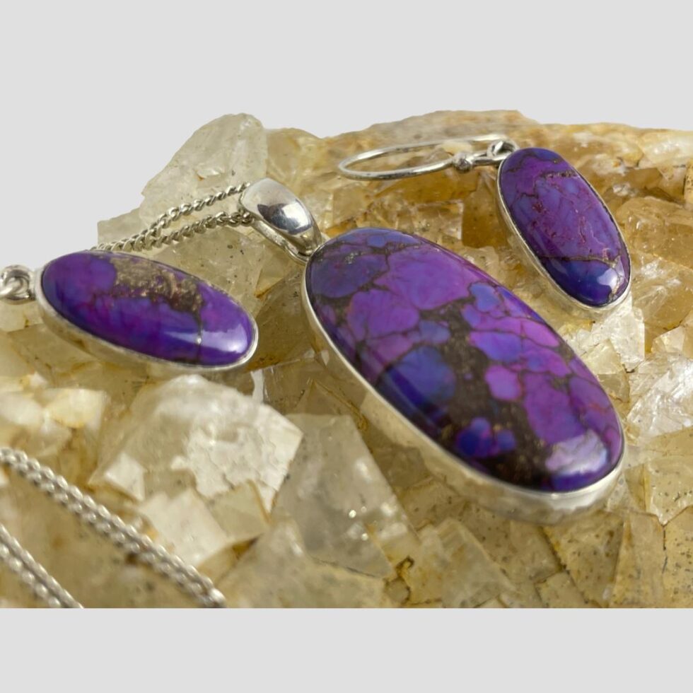 A close up photo of the pendant and earrings to highlight the beauty of the purple Mojave turquoise stones. The copper in the earring on the left is quite clearly visible here. The colour of the river quartz is a yellowy white which enhances the purple of the stones.