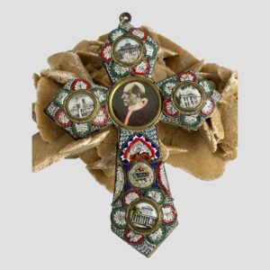Main photo of micro mosaic papal cross displayed leaning against a rock of natural desert sand rose with the cross front on display. The mosaic colours are in red, white, blue and green with round brass open locket areas at the tips with pictures of famous Roman landmarks and in the centre is the largest picture with Pope Pius XII. The collar of the popes cloak has been hand coloured a pale pink which appears a little faded with time. The mosaic is in good order and nearly all present.