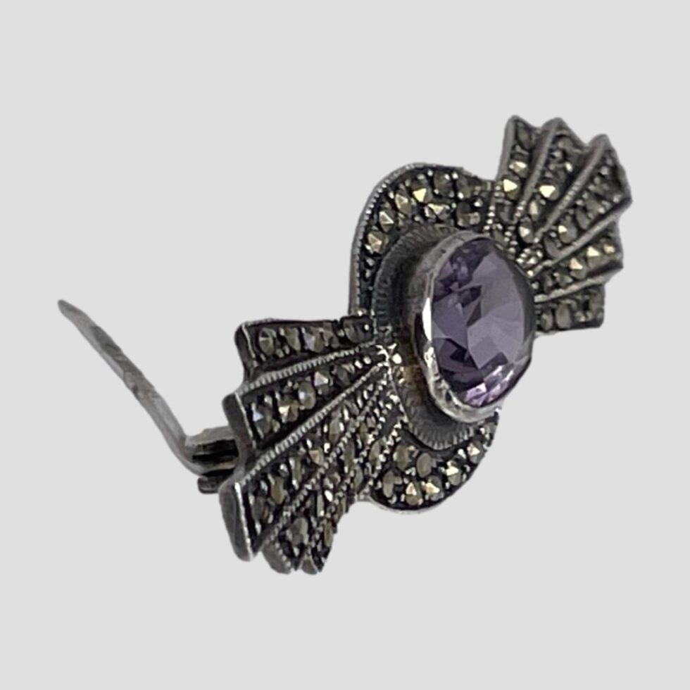 Photo of Deco style amethyst silver brooch displayed propped upright by its own pin with the brooch front facing towards the bottom right corner.