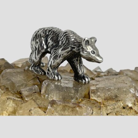 Main photo of miniature sterling silver bear displayed on top of a rock of natural river quartz with the bear facing toward bottom right corner. The whole righthand side of the bear is visible. The way it has been created makes the bear appear to be in motion. Rather a fabulous piece with good detail.