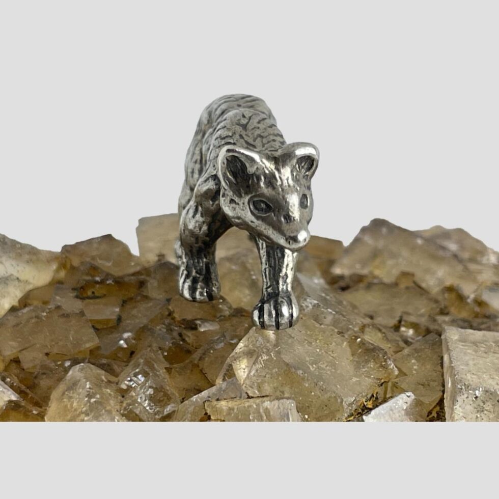 Photo of miniature silver bear still displayed on the river quartz this time with the bear forward facing with just its head, front paws and spine visible as if walking towards the camera.