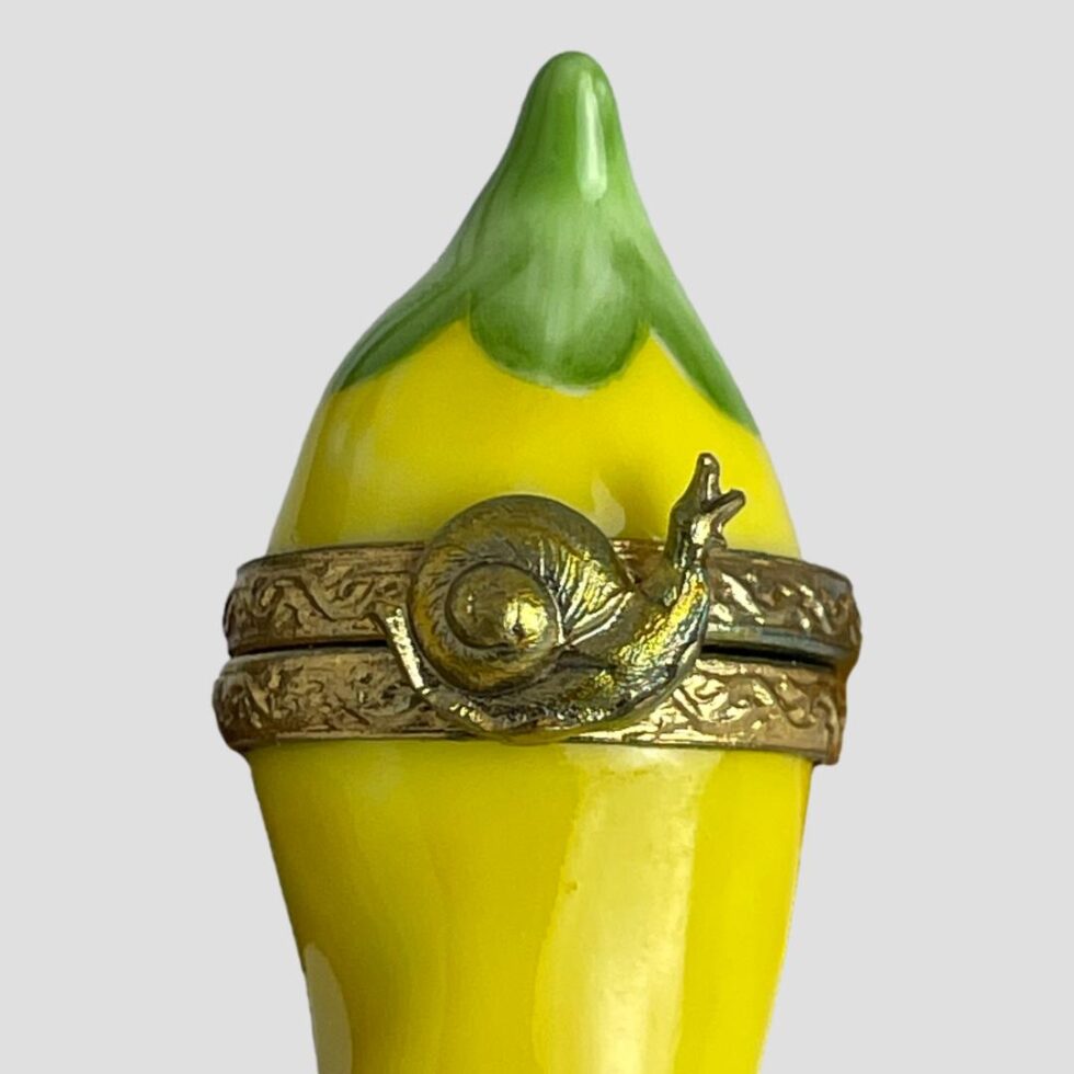 Close up photo of the the brass band opening area of the Limoges chilli box. The band has some swirly decorative patterns with the snail marking the opening point of the lid. Recommend to open at the band and not the snail.