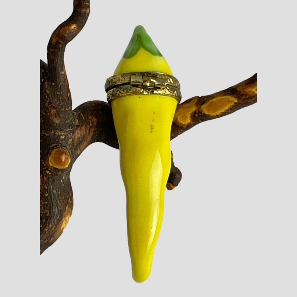 Photo of the back of the Limoges yellow chilli box showing the hinge area of the band . The chilli is still leaning against the twig.