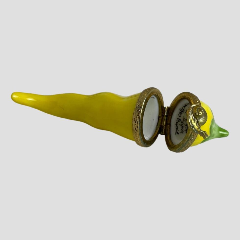 Photo of the yellow chilli box by Limoges laid horizontally flat with the pointed end on the left and the lid shown open and the signature just visible.