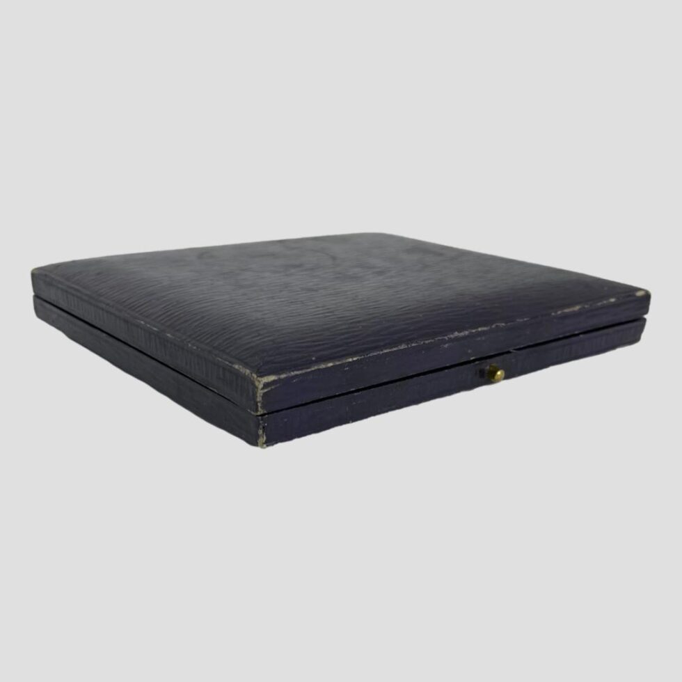 Photo of the original case shown closed with the opening front side in the bottom right corner. The case is a dark navy blue and some scuff marks are visible although quite minor for an item of this age.