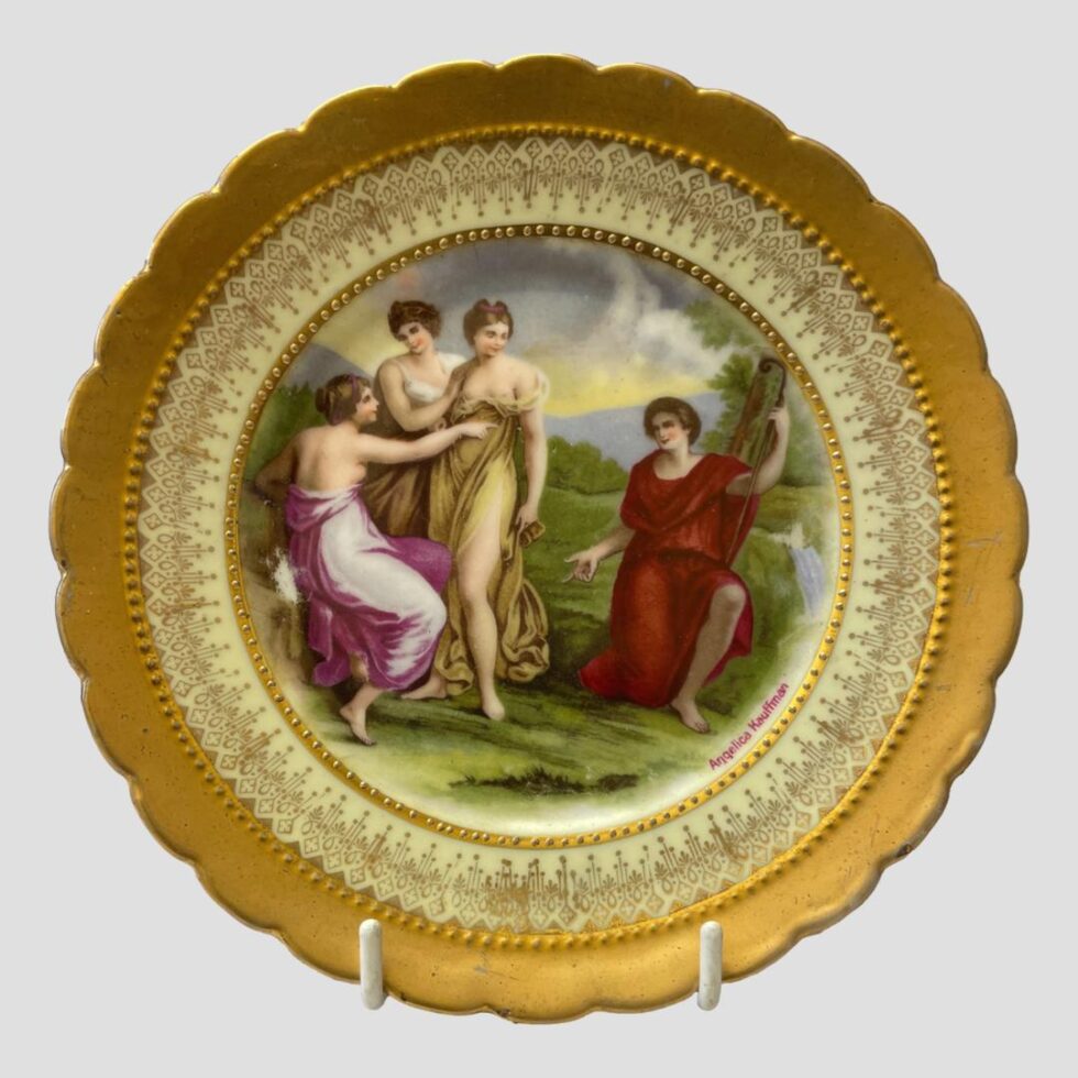 Close up photo of the neo classical style plate with the bathing beauties. On the left are 3 young ladies, 2 standing, 1 seated either dressing or undressing (one has both breasts out. These ladies are dressed in golden or pink dresses. On the right and down on one knee is an older lady in bright red with a shepherds crook in hand. It's quite am interesting scene from which many stories could be told from! Paint wear is visible to left (behind the bottom of the girl in pink) and to the right (just above the waterfall behind the woman in red.