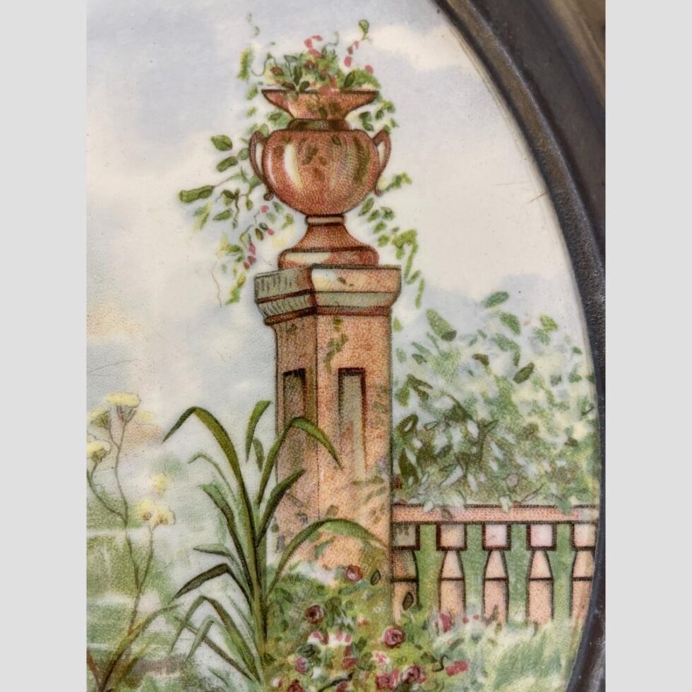 A close up image of an urn with green leaved pink flowered plant flowing from it. It is the only urn in the image and sits to the right of the young man.