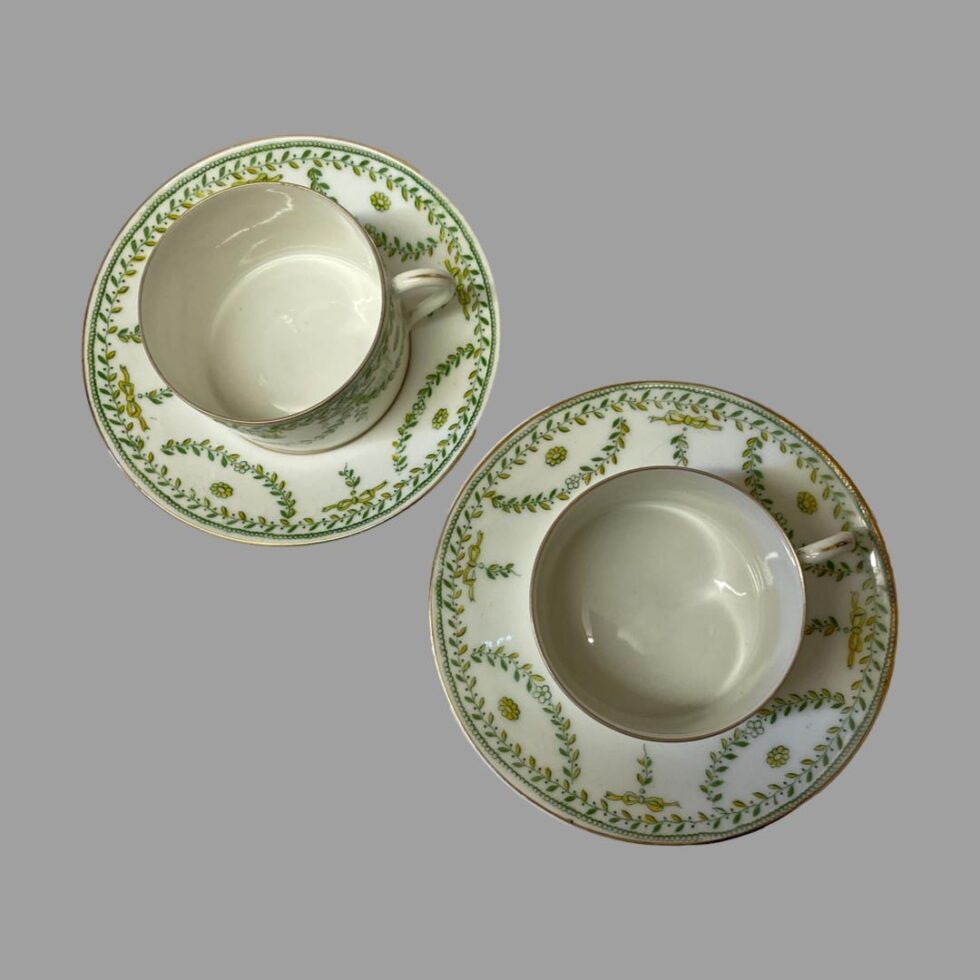 Photo looking straight down at both cups on top of their saucers from above. The garland pattern continues around the outer edge of the saucers.